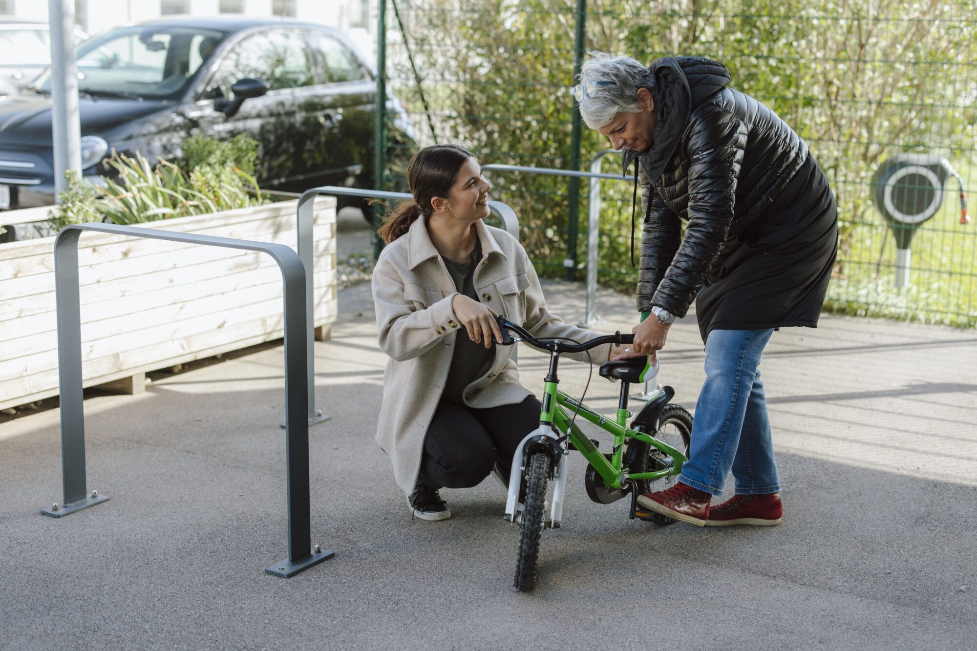 Auf dem Bild sind eine &auml;ltere Damen und ein junges M&auml;dchen zusehen, die beide ein gr&uuml;ner Kinderfahrrad begutachten.