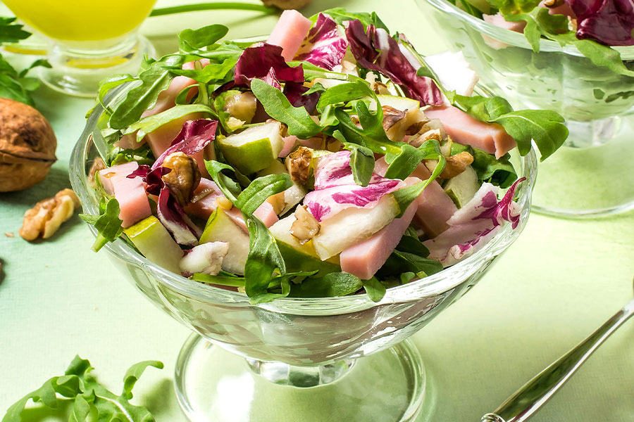 Glasschüssel mit bunten Salat. Sichtbar sind Birnenstücke, Schinkenstücke und Rukolablätter