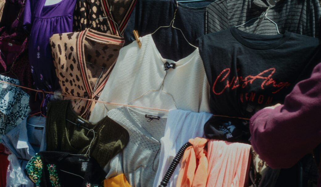 Viele unterschiedlich bunte Kleidungsst&uuml;cke h&auml;ngen auf W&auml;scheleinen gespannt auf einem Flohmarkt